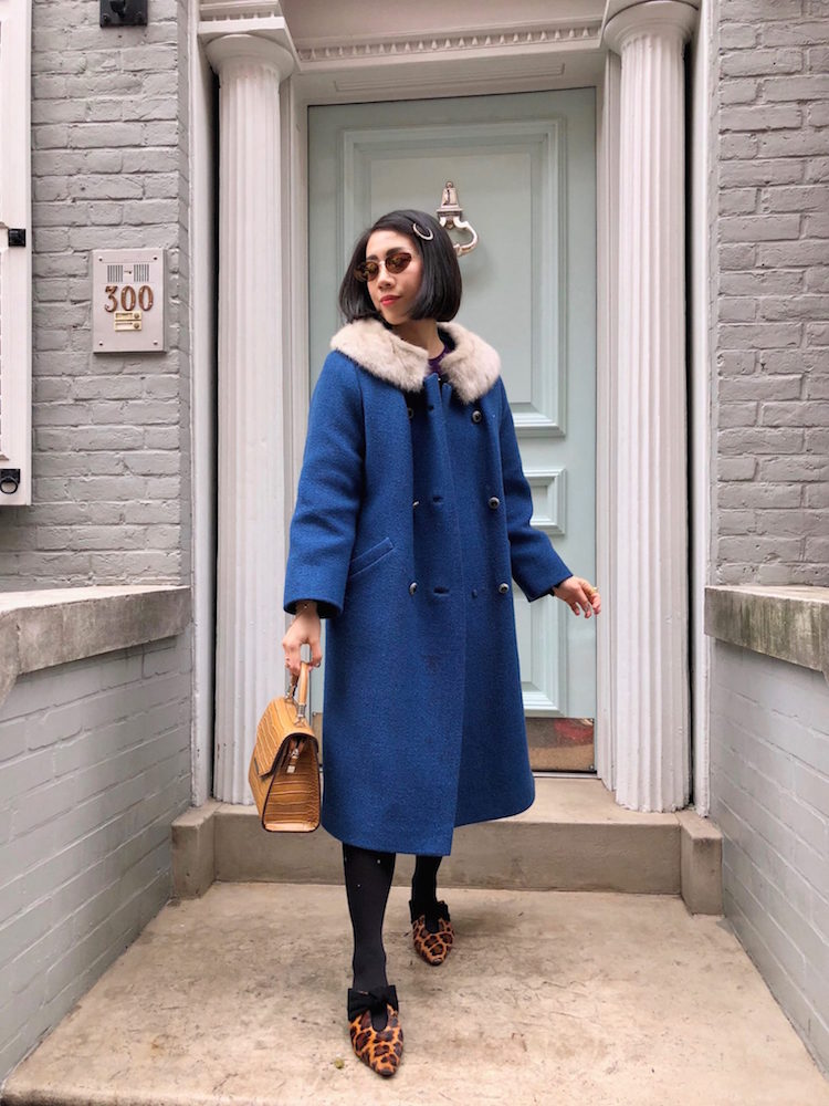 Wendy Sy vintage shopping in New York City wearing a dark blue coat, sunglasses, leopard flats, and a brown bag.