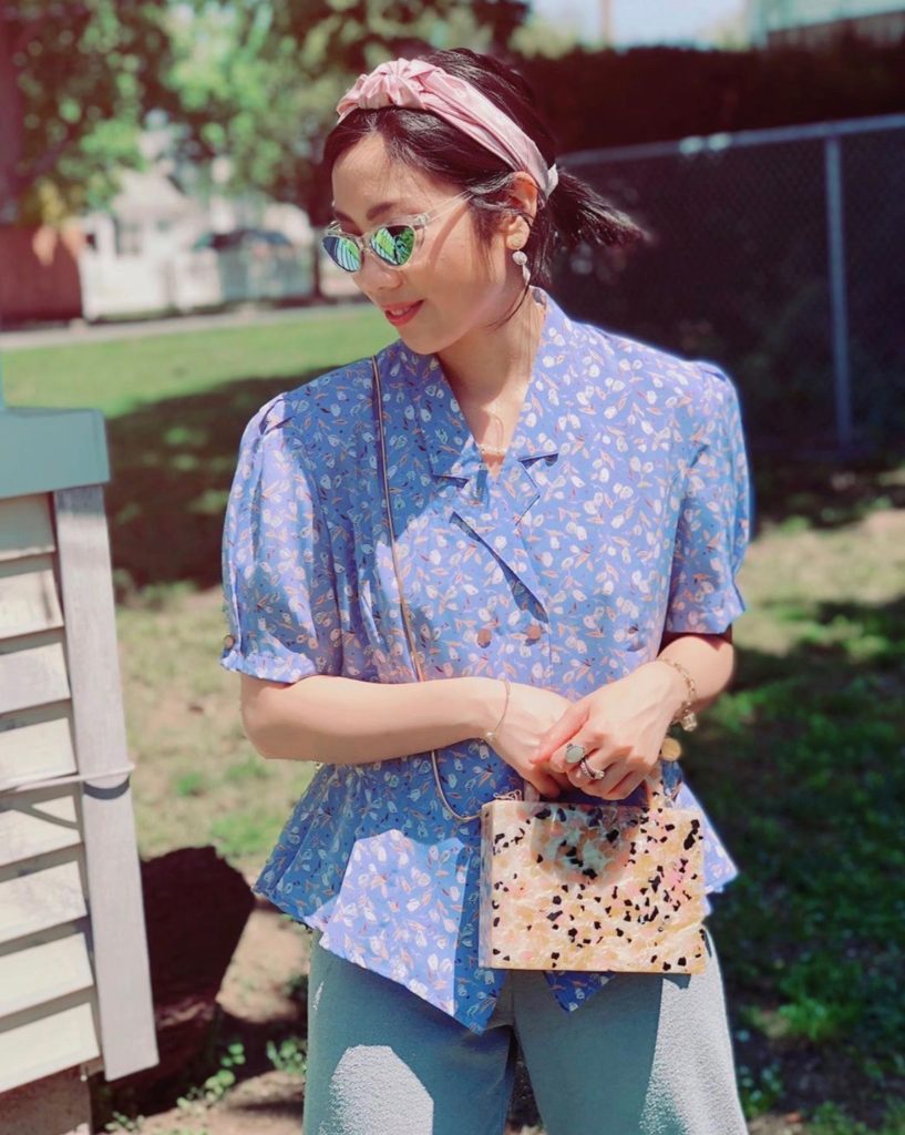 Girl wearing a vintage blue floral top, sunglasses, pink headband, and printed handbag as a quarantine outfit.