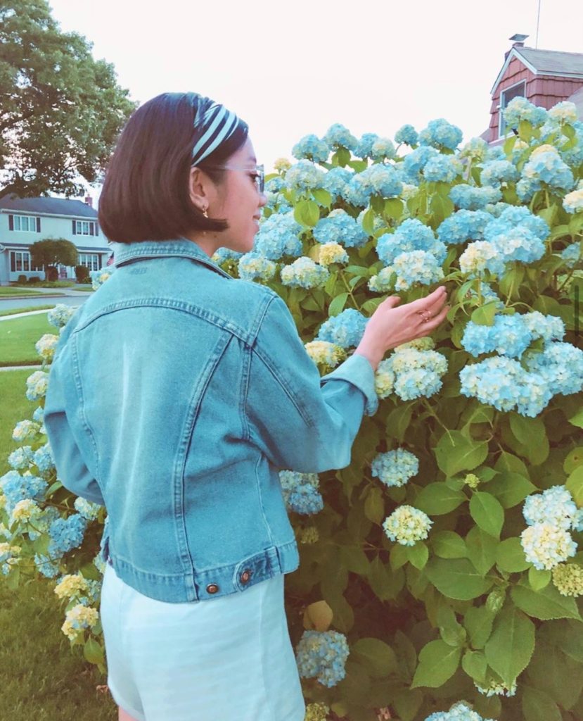Girl wearing a vintage denim jacket, and striped headband with a backdrop of blue hydrangeas.