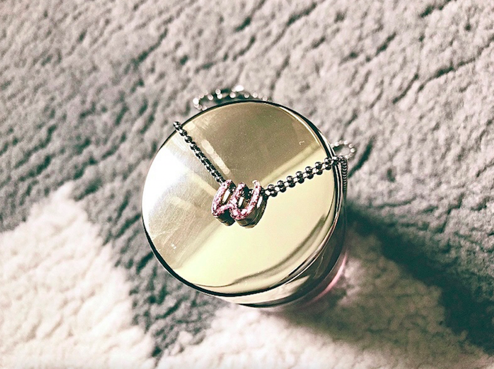 Silver Alex Woo necklace with a pink W initial charm on top of a Smith & Cult round nail polish bottle cap.