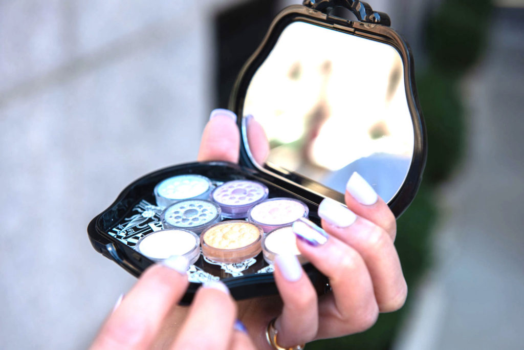 Hands with purple nails holding an Anna Sui Cosmetics eyeshadow palette in Gramercy Park, New York.