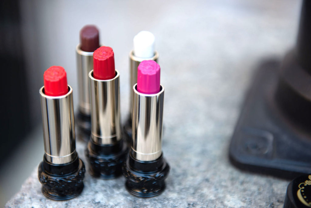 Five lipsticks in various colors on a gray marble countertop.