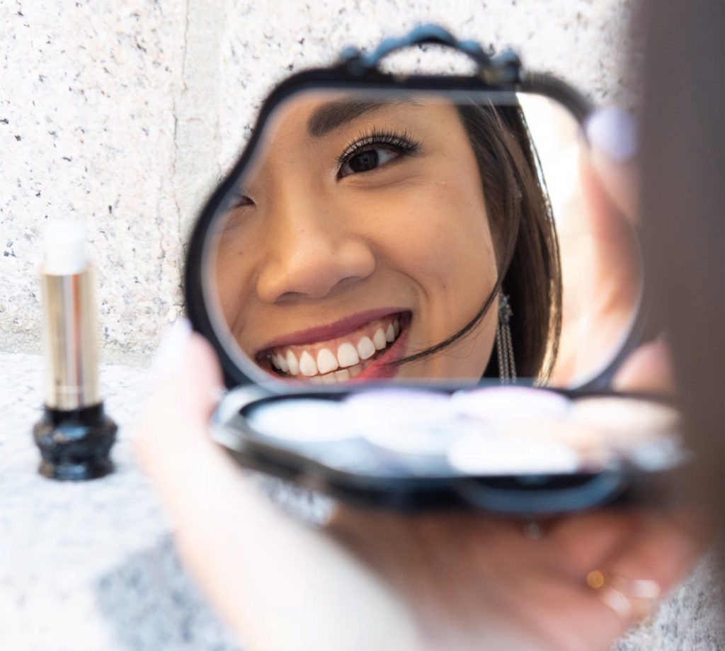 Wendy Sy looking into a reflection of an Anna Sui Cosmetics eyeshadow palette outside in Gramercy Park, New York.