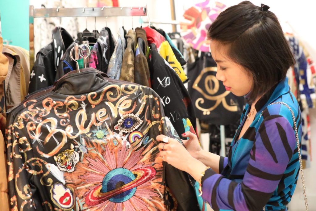 Wendy Sy holding a black leather jacket with hand-painted designs by DAFNE Italy during Miami Art Basel events.