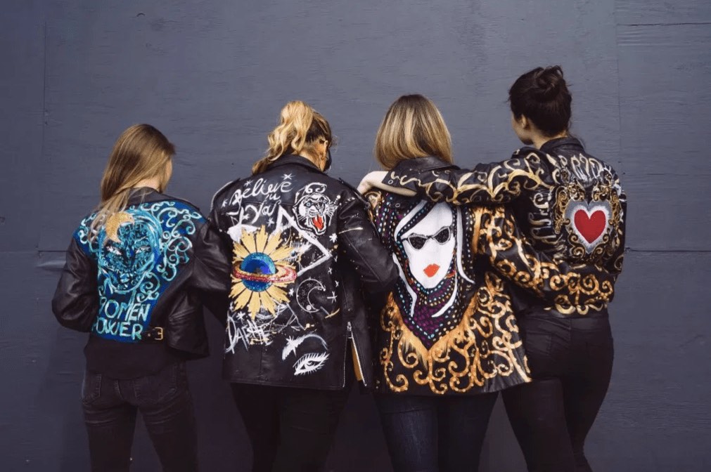 Four women wearing black leather jackets with colorful hand-painted designs by DAFNE Italy, who shares top fashion career tips.