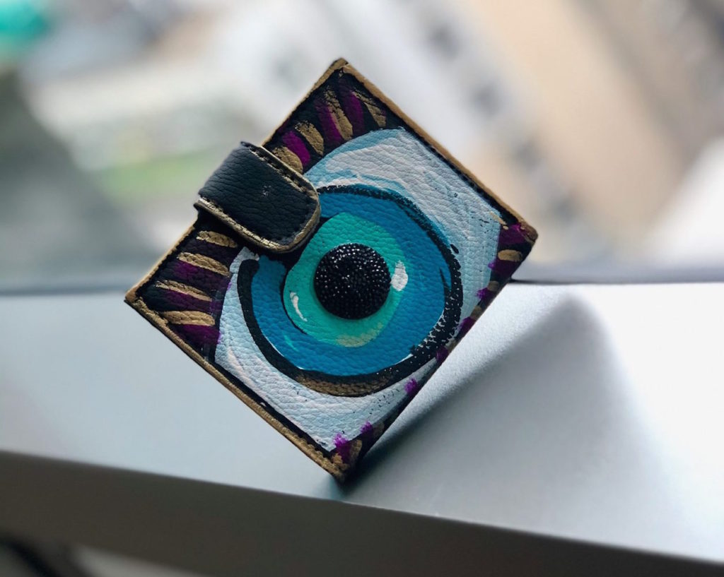 Diagonal shot of a black wallet with a blue and white eye hand-painted print by DAFNE Italy, who shares top fashion career tips in this post.