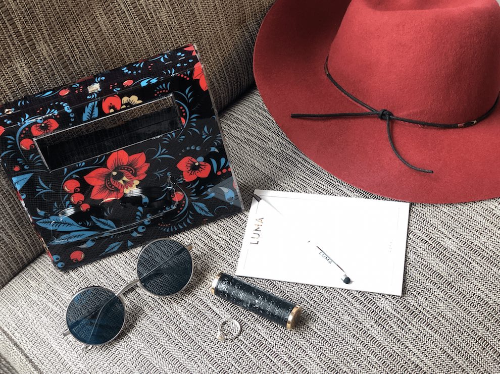 Floral purse, sunglasses, red hat, lipstick, ring, and a notepad on a couch.