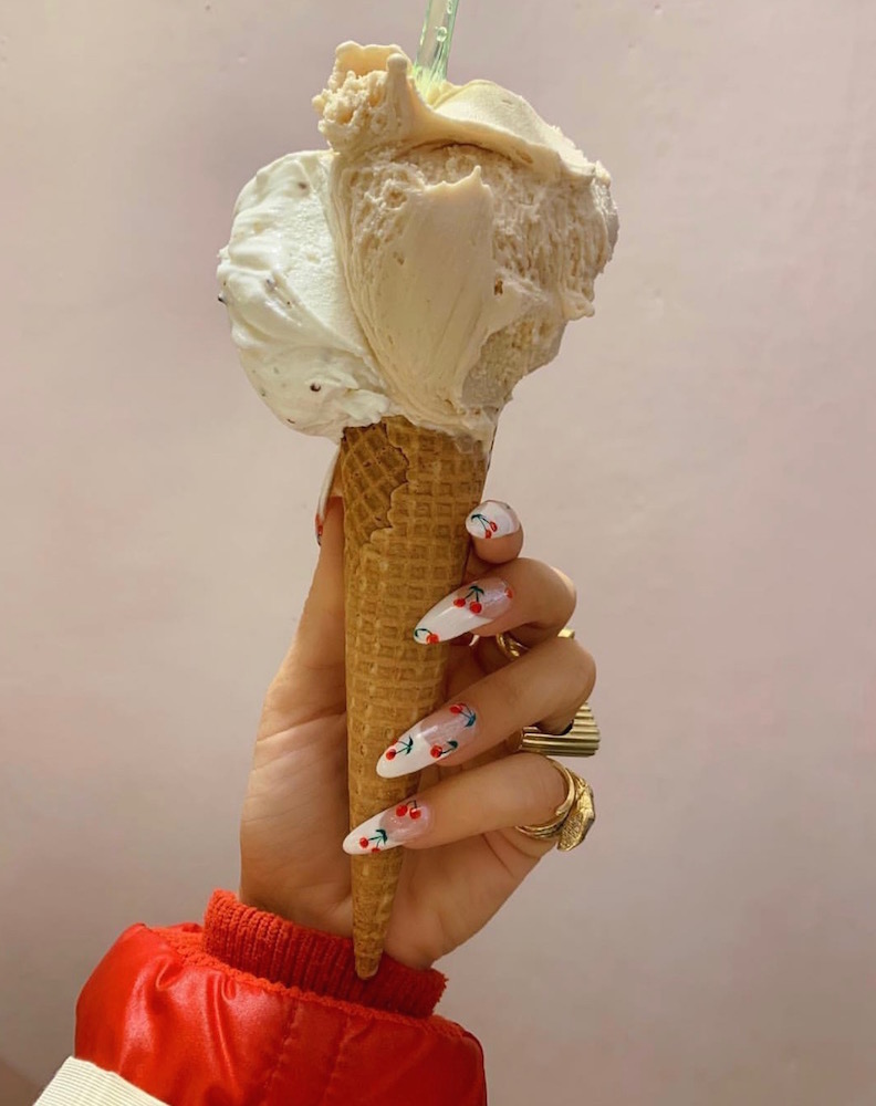 A hand holding a vanilla ice cream cone with long cherry design nail art by Rose B. Nails with Leafgel products.