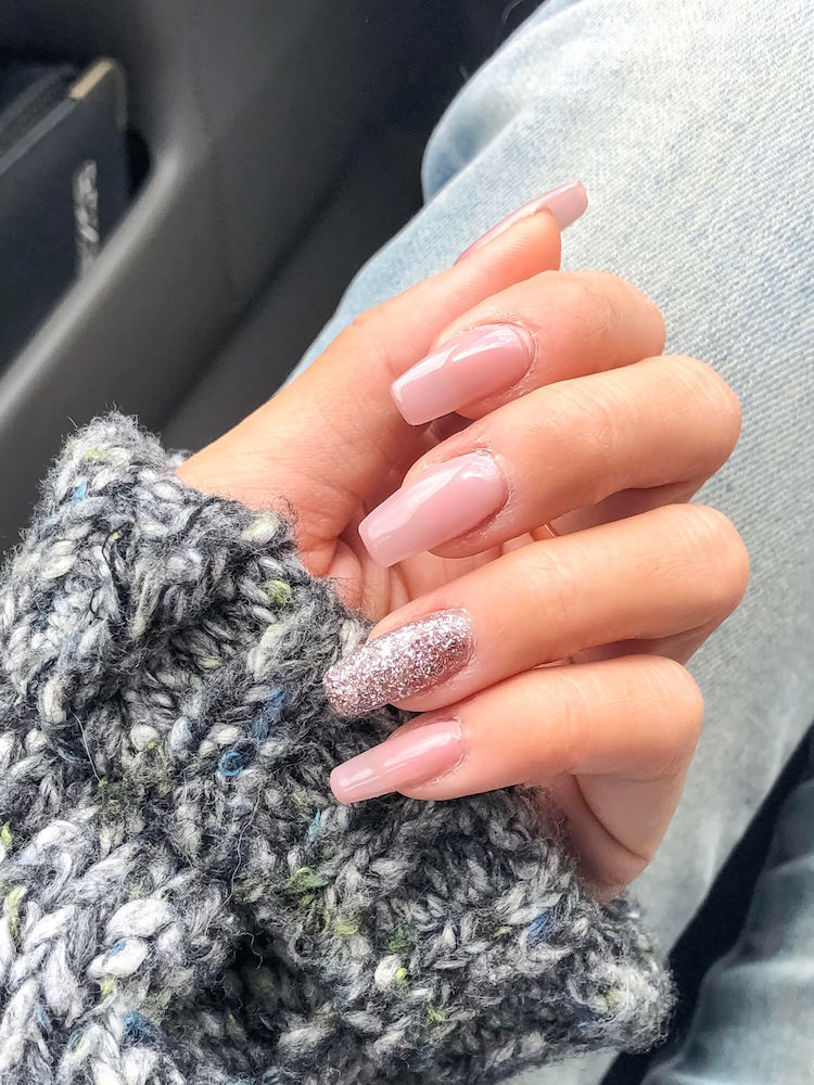 One hand with light pink and glitter nail polish by VW Nail Bar holding onto a dark gray sweater.
