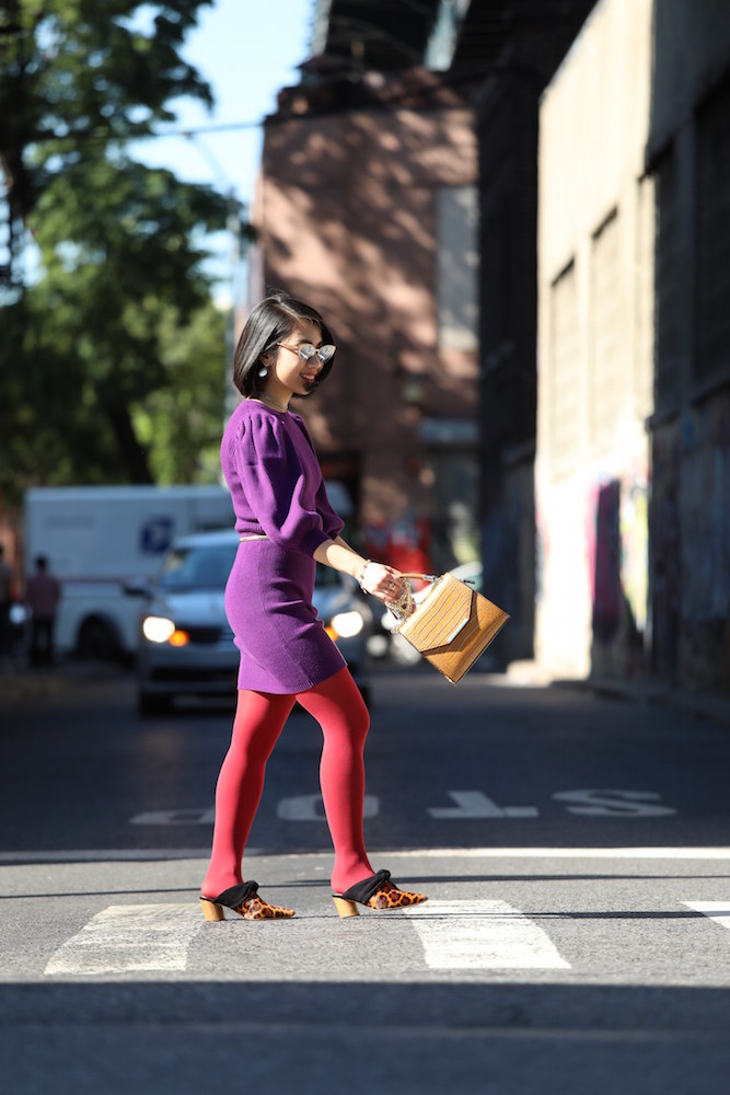 Wendy Sy wearing red tights, a purple dress, and brown bag crossing the street in New York City.