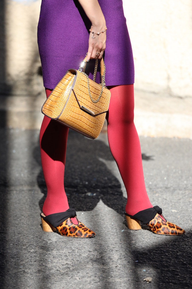 National Legwear Day in red L'egg tights, a purple dress, and brown bag outside in New York City.