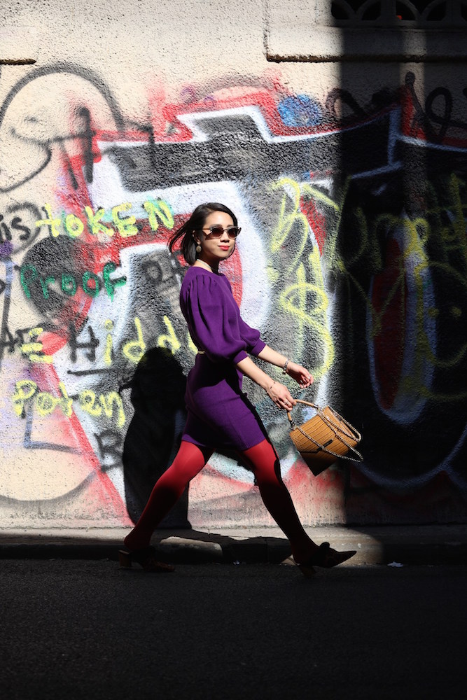 Wendy Sy wearing red tights, a purple dress, and brown bag outside in New York City.