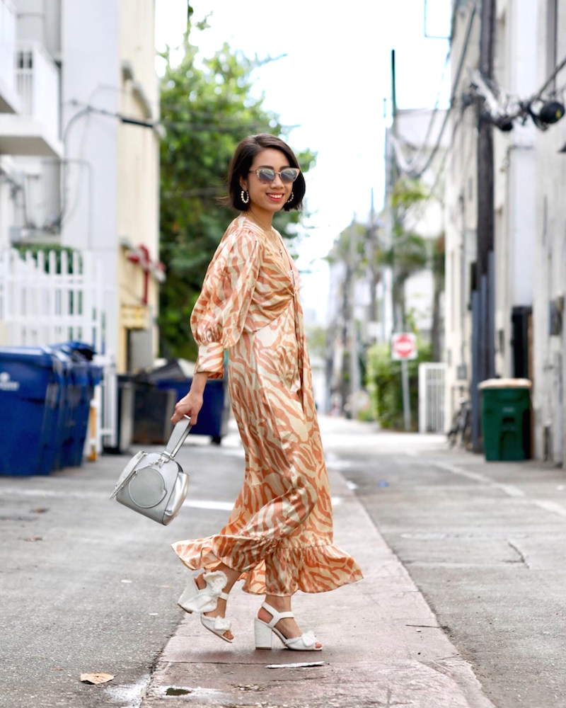 Wendy Sy wearing a orange zebra printed dress with white sandals and a gray bag outdoors in Miami.
