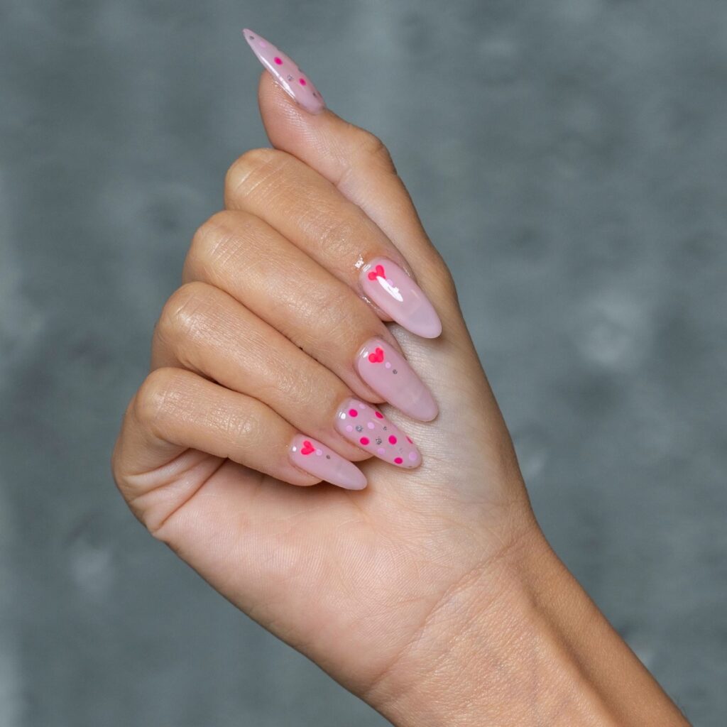 valentine's day nails with a light pink base and dark pink hearts and polka dots.