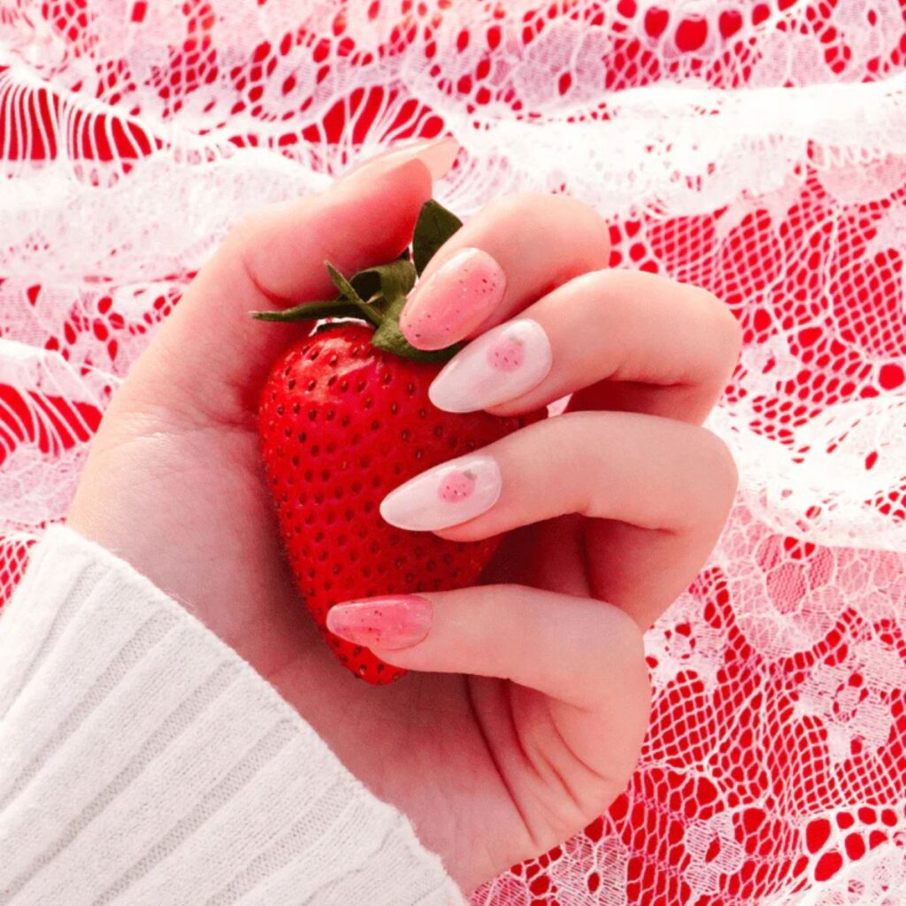 Hand with pink strawberry nails with a red and white lace background.