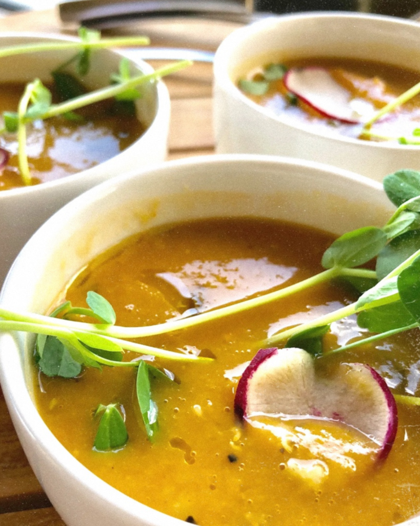 Three white bowls of vegetable soup at the wellness center with green vegetable garnish on top.