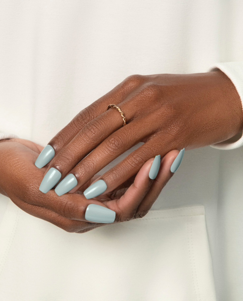 Two hands with a light green press-on manicure with a cream color background
