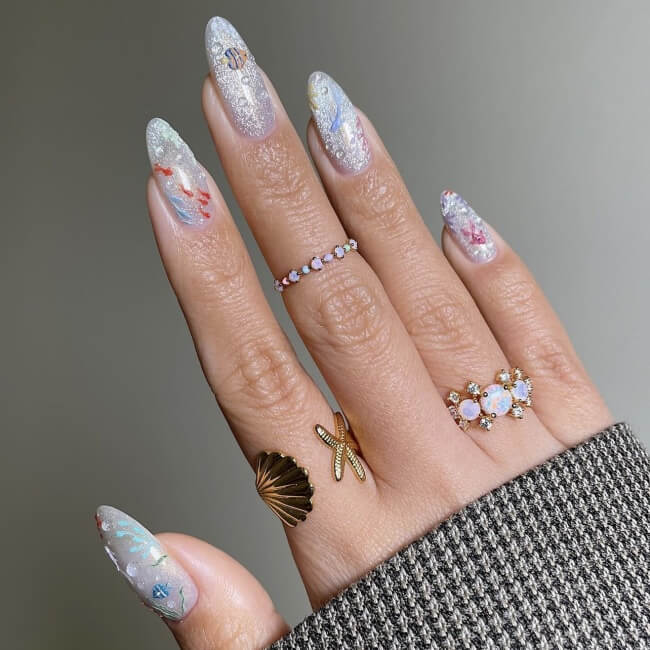 Fingertips with light blue sparkly beach nails and iridescent rings.