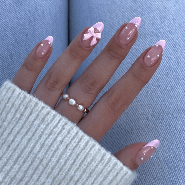 A hand showing French tips, a pink bow and white pearls on a backdrop of light wash denim