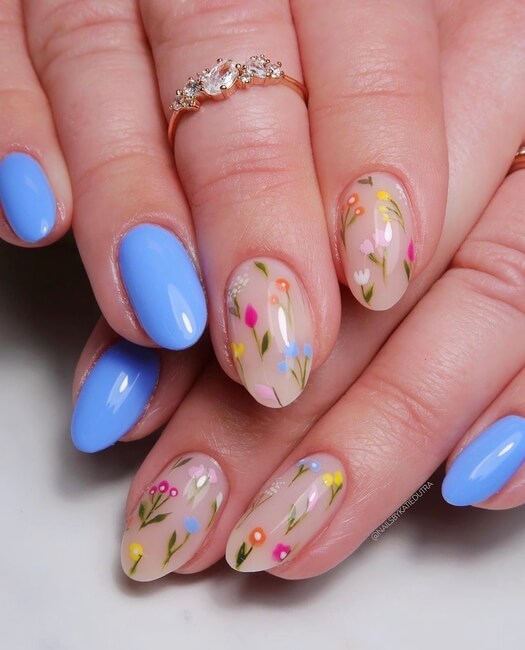 Two hands stacked featuring light blue nail polish and colorful dainty floral designs