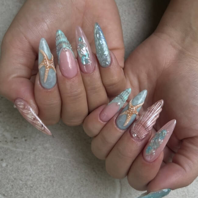 Almond beach nails with light blue shades and seashells on two hands.