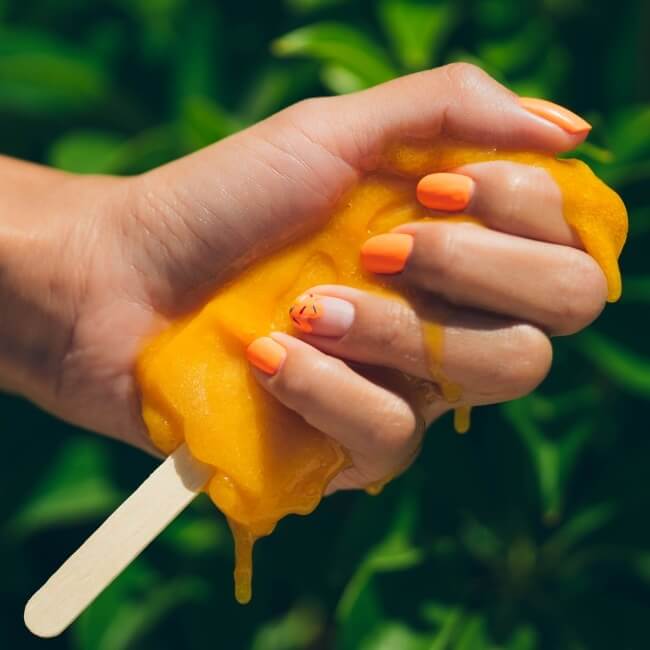 Short summer nails with a bright orange color holding a popsicle in the same color