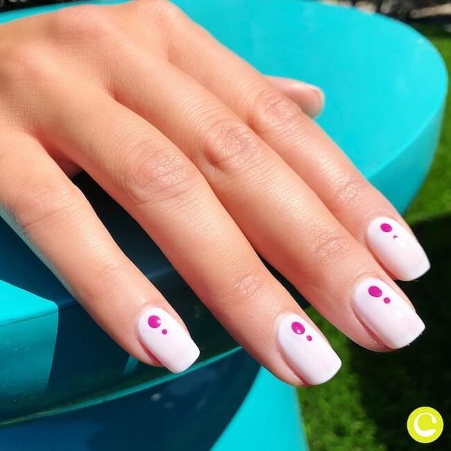 One hand with a solid light purple manicure and two darker purple polka dots on each nail