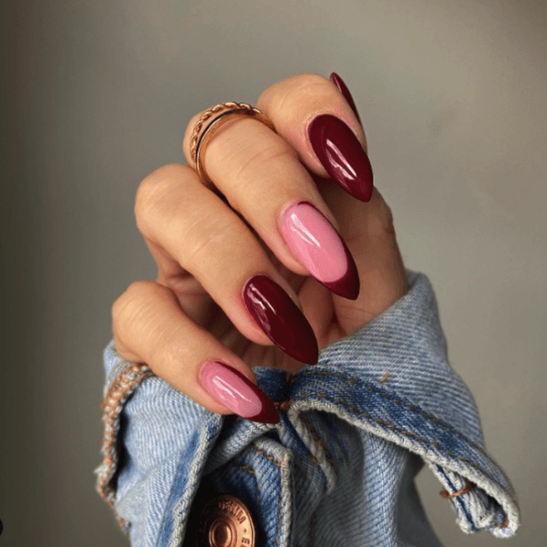 A hand with deep burgundy and pink manicure with a denim jacket sleeve