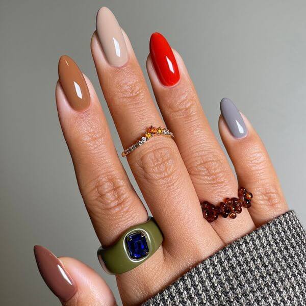A hand with a multi-colored fall nails on a gray background