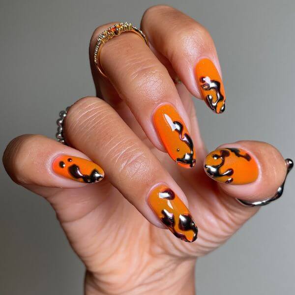 A hand with orange and metallic nail polish for Halloween nails ideas