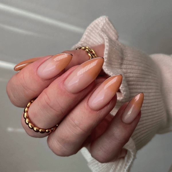 A hand with nude nails almond manicure with a cream sweater sleeve