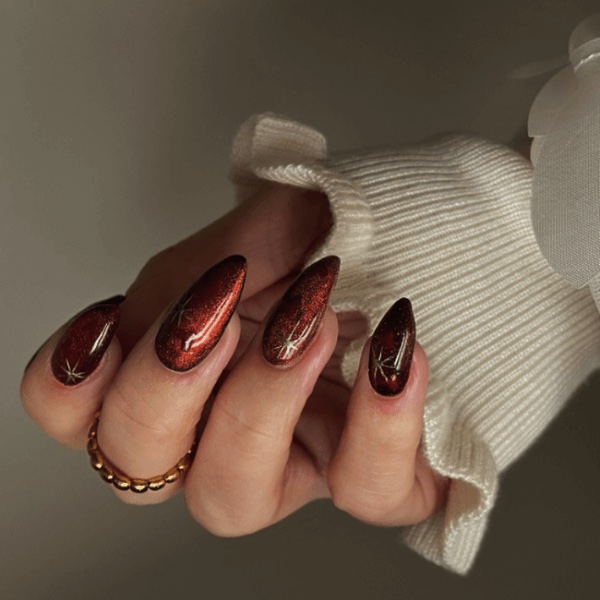 Dark burgundy September nails peeking from a cream sweater sleeve.