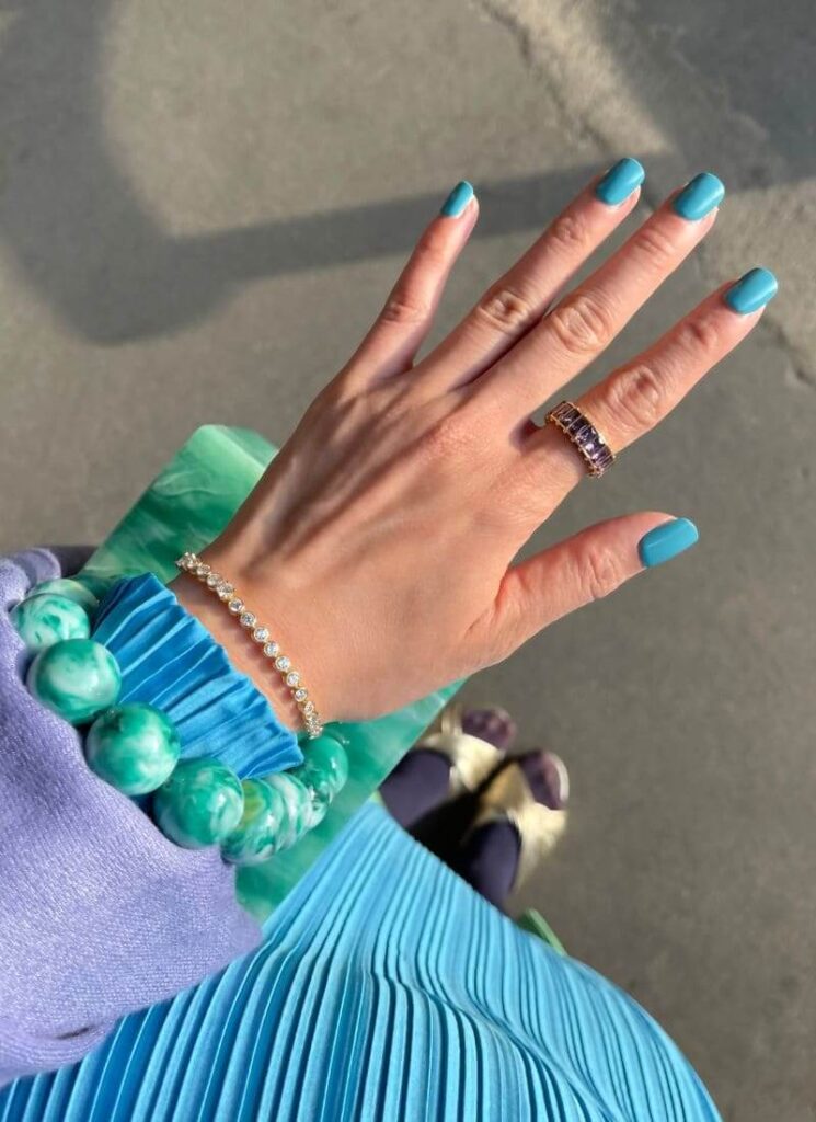 Detail shot of a turquoise manicure with the same color dress and green bag