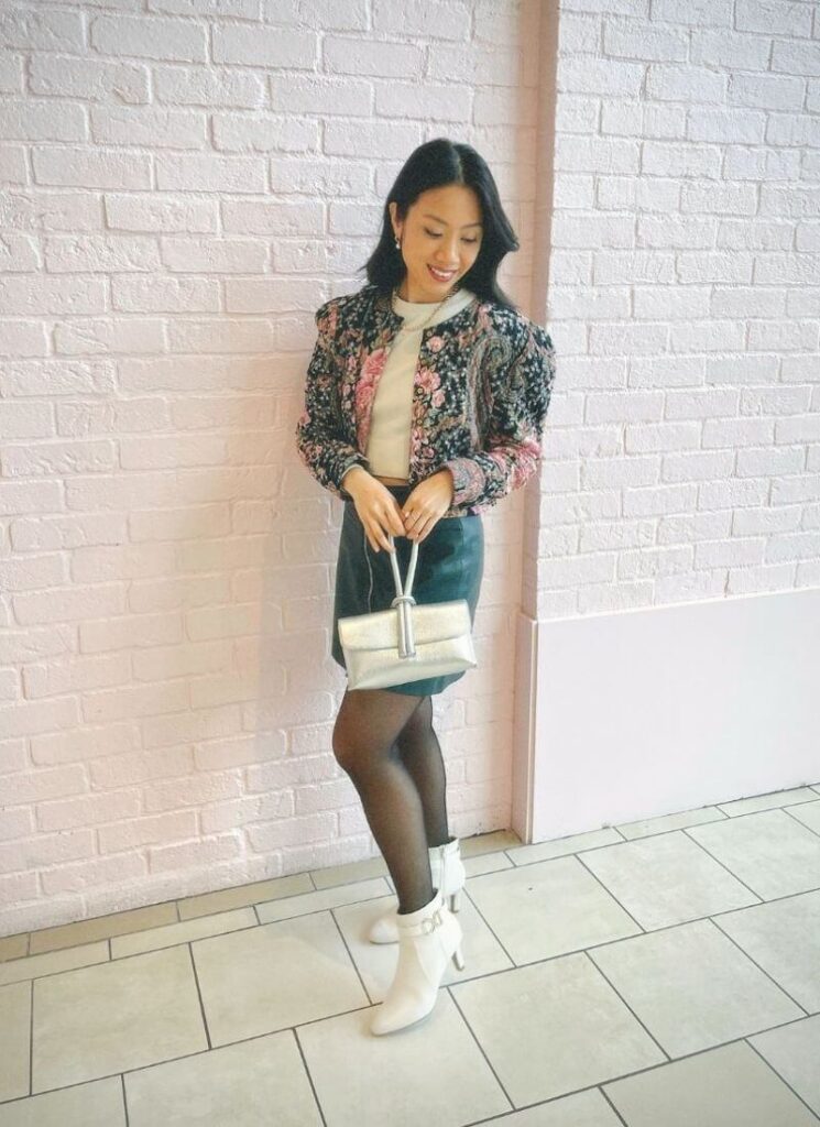 Autumn outfit with a quilted jacket, mini skirt, tights, and white shoes with a pink background.