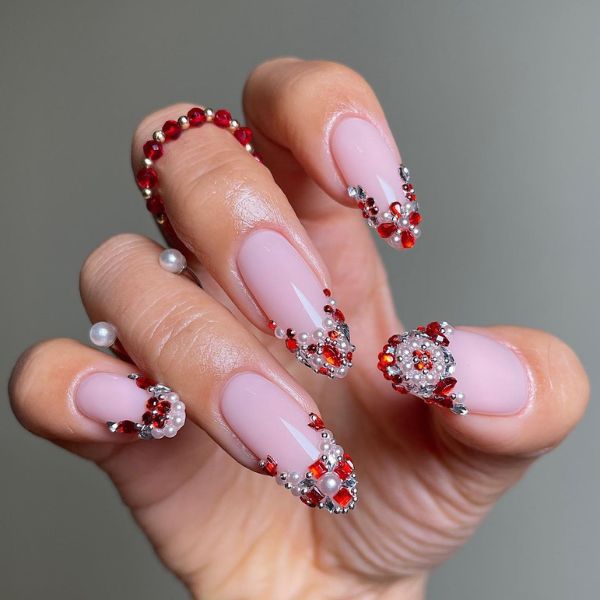 Pink Christmas nail designs with red diamonds and white pearls on a gray background