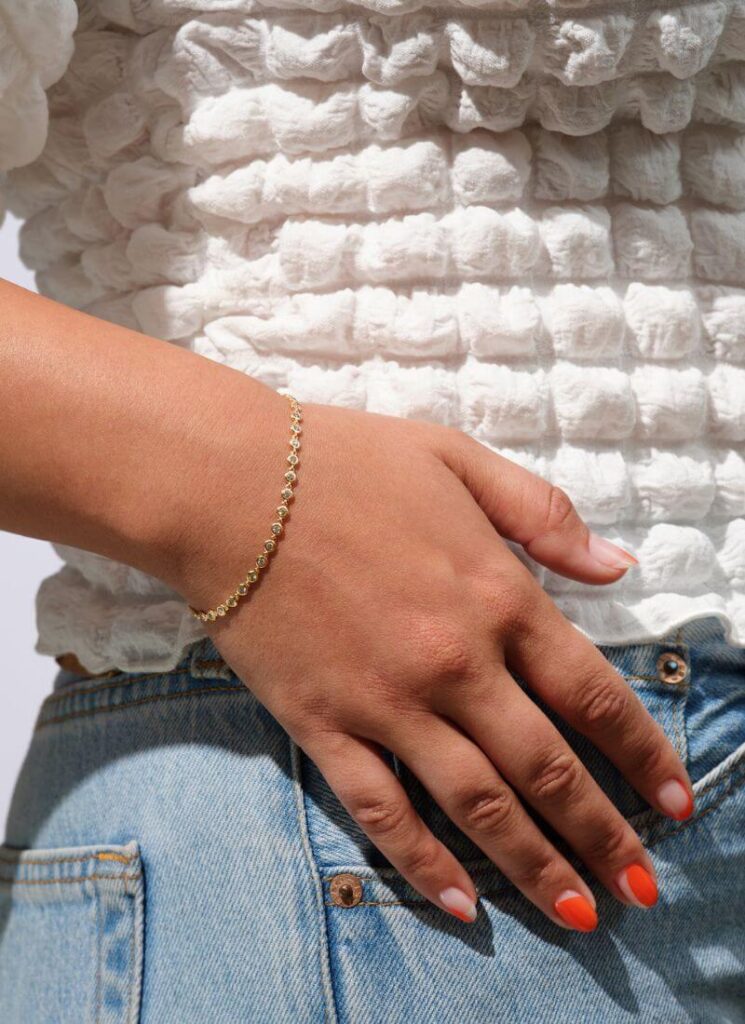 A hand with a silver permanent bracelet with a white top and blue jeans