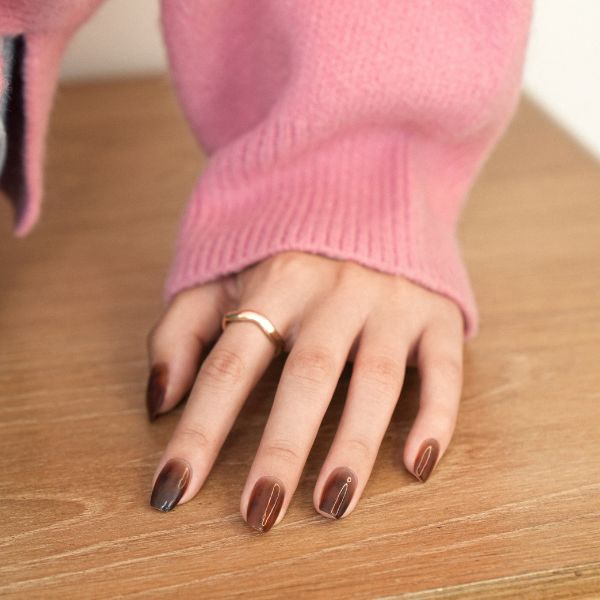 espresso nails with a pink sweater sleeve and wood background.