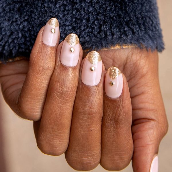 Close up of gold glitter nails on a beige background.