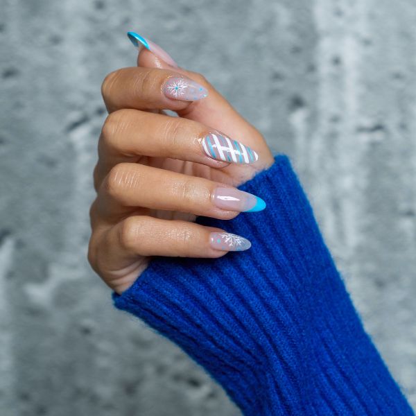 snowflake nail designs with a blue sweater sleeve and gray background.