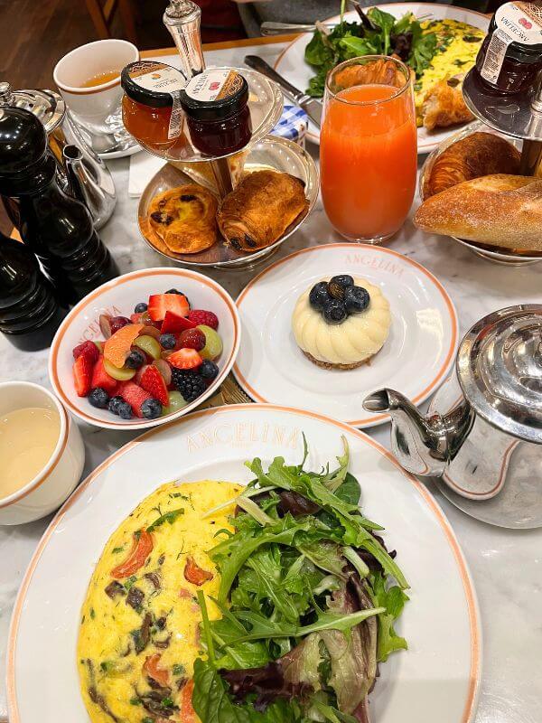 Afternoon tea setting with teacups, fruit bowl, omelet, and pastries at Angelina Paris New York City.