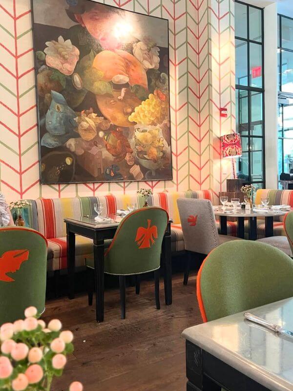 Interior of The Crosby Street Hotel with a colorful patterned wallpaper, green chairs, and dining tables.