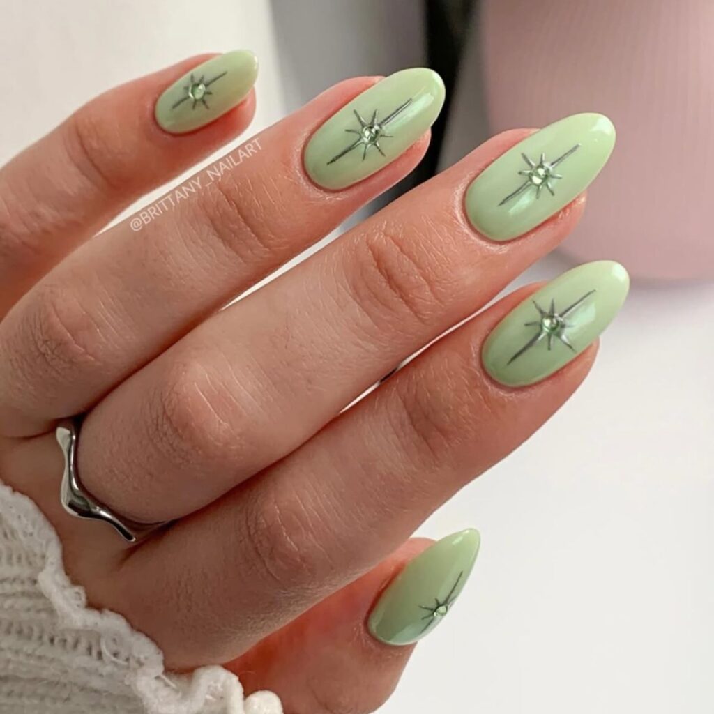 A close-up of a hand with light green spring nails with sparkle embellishments on a white background.