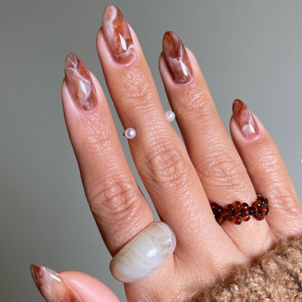 Brown and white coffee nails with a pearl ring on a gray background.