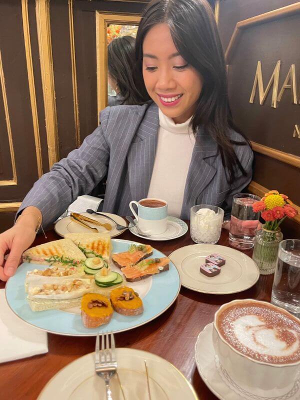 Guest at Marie Belle Cacao Bar in New York holding a plate of finger sandwiches at afternoon tea.