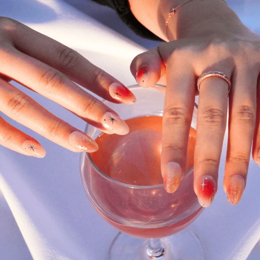Two hands holding a wine glass with a pink manicure and sparkle nail design.