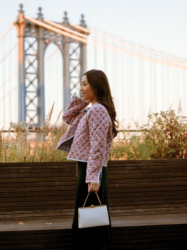 Wearing a pink floral print quilted jacket with a New York skyline background.