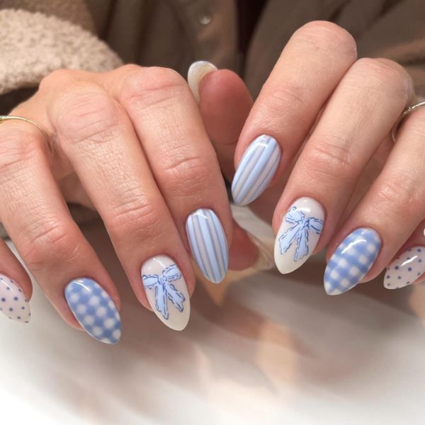 Close up of blue and white manicure with various designs including bows, gingham, and polka dots.