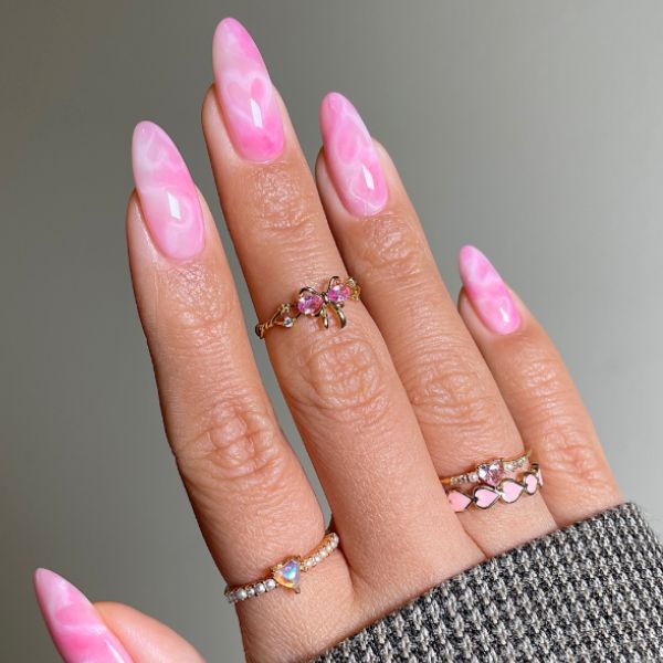 Pastel pink nails with subtle white hearts on a gray background.