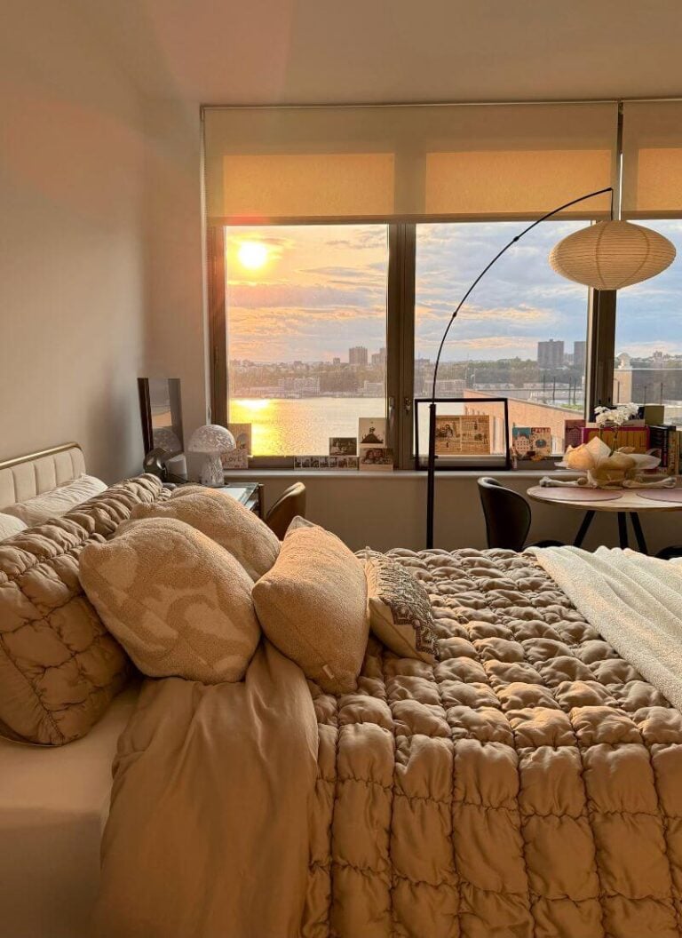 Cozy bedroom with soft lamp light, a bed by the window, and a warm sunset glow.