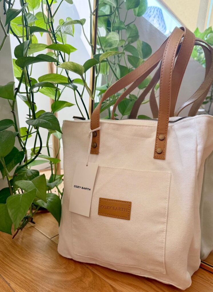 A white tote bag with brown handles with bamboo bed sheets inside.